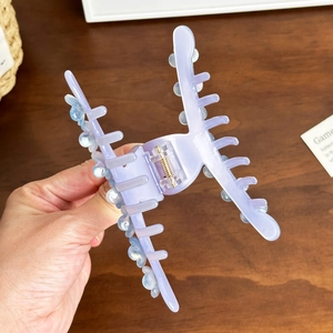 Elegant purple acetate flower claw clip with pearl accents held by a hand over a wooden table