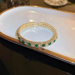 Close-up of double-row gold plated square diamond bracelet with green stones on ceramic tray