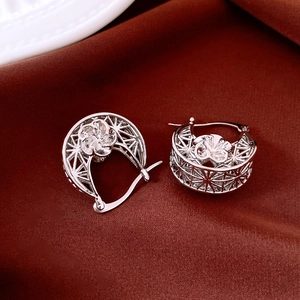 Macro shot of silver hollow-out flower hoop earrings on deep burgundy velvet background
