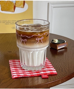Close-up of clear glass cup with pink bow pattern holding iced latte on a checkered coaster