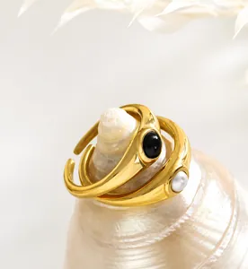 Close-up of gold-plated rings with black gemstone and pearl on white seashell decor