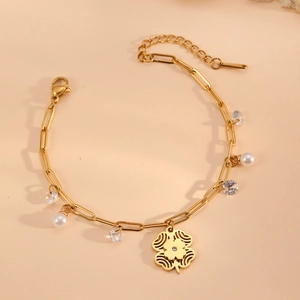 Gold-plated stainless steel bracelet with clover charm, pearls, and crystals on beige base