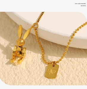 Detailed macro view of the 3D golden rabbit pendant and engraved charm on a beaded chain