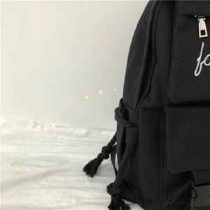 Detail of black canvas backpack with white embroidery and decorative woven side cords