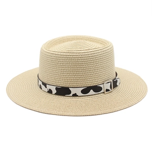 Detail view of woven boater straw hat featuring a black and white cow print decorative band