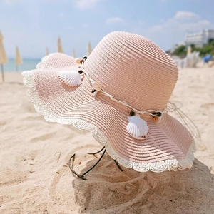 Pink straw sun hat with shell decorations and white lace trim at beach