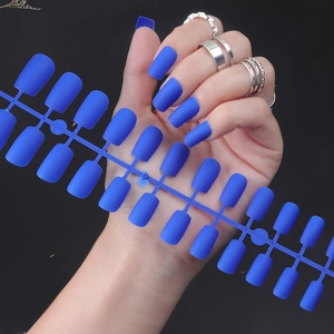 Close-up of matte blue long square press-on nails with silver rings on dark background