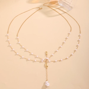 Detail of gold body chain with tiny pearls and a delicate shell pendant with drop pearl