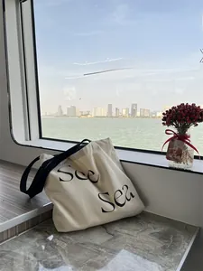 Detail of beige canvas tote bag with See Sea lettering against a scenic sea view background