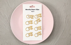 Detailed close-up of 8-piece gold pineapple-shaped metal paper clips on a pink plate