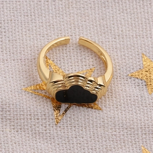 Close-up of golden adjustable ring with black enamel cloud design on textured linen