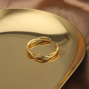 Detail of twisted gold open ring displayed on brown satin inside a golden metal tray