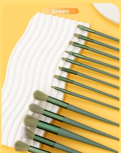 Close-up of 13 professional makeup brushes with matte green handles on textured background