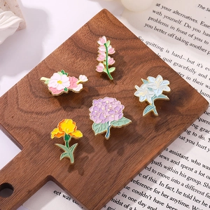 Close-up of five floral enamel pins set on a wooden plate and vintage book pages