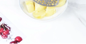 Gros plan d'un presse-purée en acier inoxydable écrasant des pommes de terre cuites