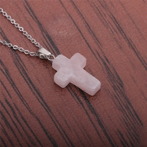 Close-up of natural rose quartz cross pendant on a thin silver stainless steel chain