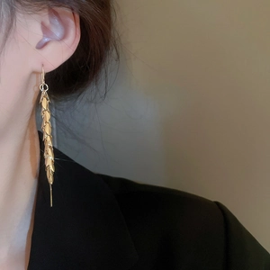 Detail of gold-plated leaf tassel earrings worn by a model showing long fringe movement