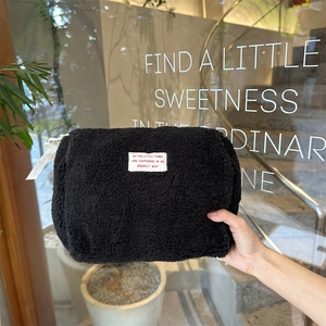 Close-up of black fleece makeup bag with zipper and white label in a hand-held view