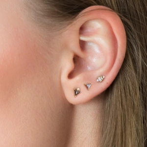 Close-up of geometric silver cartilage earrings with clear crystals on ear