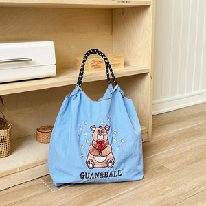 Close-up of the delicate brown bear embroidery on a light blue nylon tote bag