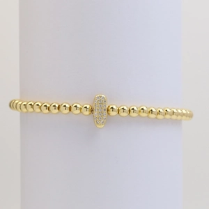 Macro shot of gold beaded bracelet with a zircon-encrusted oval pendant on a white stand