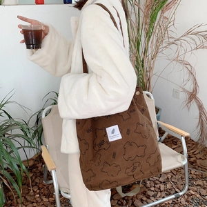 Close-up of brown corduroy tote bag with bear pattern worn by a model in outdoor setting