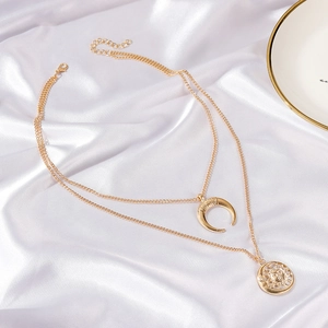 Detail of layered gold sun and crescent moon necklaces on a white silk background