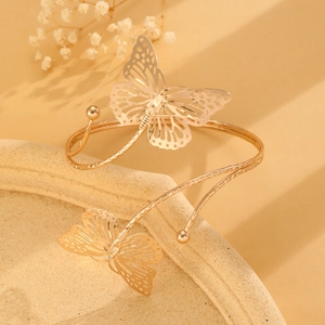 Detailed view of a golden hollow butterfly arm cuff on a textured ceramic vessel