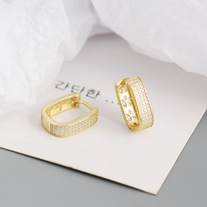 Detailed close-up of U-shaped gold earrings with paved zircons and hollowed petal sides