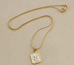 Detail of 18K gold snake chain with a rectangular shell pendant featuring letter N