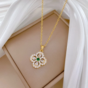Macro detail of gold four-leaf clover pendant with green zircon and pavé crystals