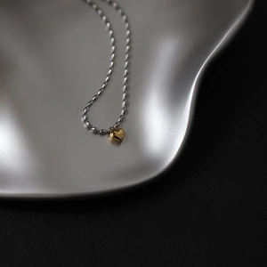 Macro detail of a golden heart pendant on a silver ball chain over a black textured base