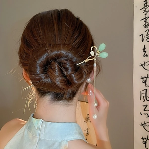 Détail d'un pic à cheveux chinois avec pétales verts et pompons en perles sur chignon