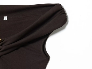 Dettaglio del tessuto a maglia marrone scuro con scollo increspato e anello in metallo oro