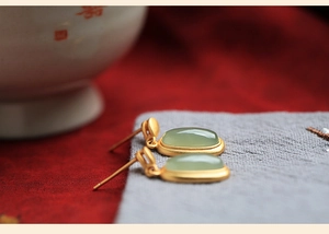 Macro detail of Chinese style drop earrings featuring matte gold finish and oval jade stones