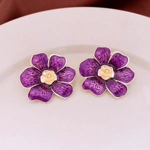 Macro shot of purple enamel flower earrings with a golden rose center on a ceramic tray