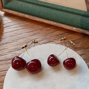 Detailed view of red cherry-shaped earrings with gold stems on a white ceramic tray