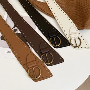 Close-up of vintage leather belts with brass studs and round buckles in multiple colors