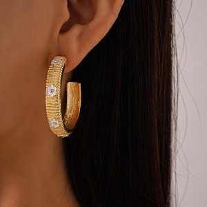 Detail of gold C-shaped hoop earring featuring white enamel flowers and crystal accents