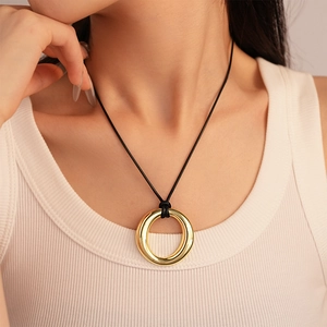 Close-up of minimalist gold circular pendant on a black cord necklace worn by a model