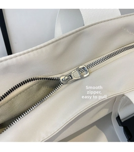 Close-up of smooth metal zipper and silver shield puller on the white canvas handbag