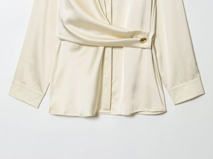 Détail d'un chemisier en satin champagne avec plis à la taille et bouton doré chic