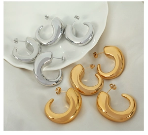 Detailed close-up of thick C-shaped hoop earrings in polished gold and silver finishes
