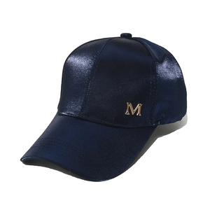 Close-up of a navy blue satin baseball cap with a metallic gold M emblem on front