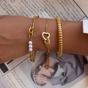 Close-up of gold stainless steel bracelet set with pearls and interlocking heart charm