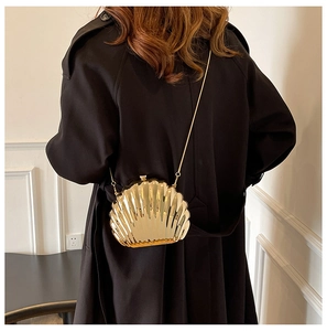 Golden shell-shaped evening clutch bag with chain strap shown against a black coat