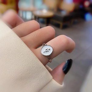 Detailed view of a round white shell ring with a silver floral bud center on a finger