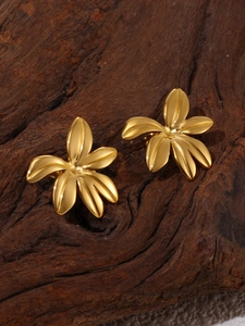Macro view of gold flower stud earrings on textured dark wood background