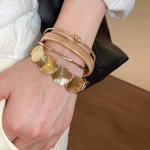 Close-up of four-piece gold irregular round bracelets set on model's wrist with metallic texture