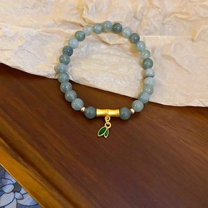 Close-up of aquamarine camellia beaded bracelet with gold bamboo joint and green leaf charm